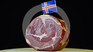 Delicious smoked tenderloin with small flag of Iceland, piece of meat rotating on balck background.