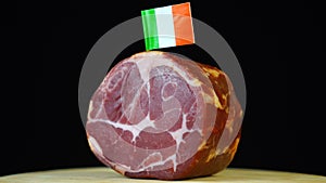 Delicious smoked tenderloin with small flag of Ireland, piece of meat rotating on balck background.