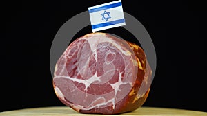 Delicious smoked tenderloin with small flag of Israel, piece of meat rotating on balck background.