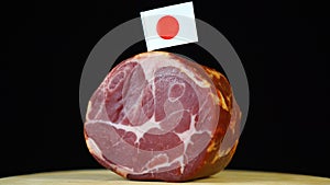 Delicious smoked tenderloin with small flag of Japan, piece of meat rotating on balck background.