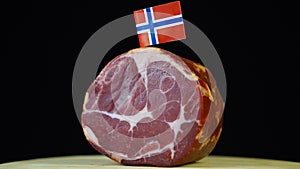 Delicious smoked tenderloin with small flag of Norway, piece of meat rotating on balck background.