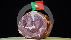 Delicious smoked tenderloin with small flag of Portugal, piece of meat rotating on balck background.