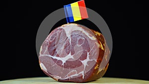 Delicious smoked tenderloin with small flag of Romania, piece of meat rotating on balck background.