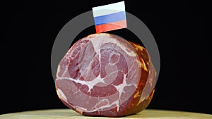 Delicious smoked tenderloin with small flag of Russia, piece of meat rotating on balck background.