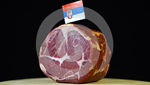 Delicious smoked tenderloin with small flag of Serbia, piece of meat rotating on balck background.