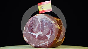 Delicious smoked tenderloin with small flag of Spain, piece of meat rotating on balck background.