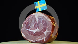 Delicious smoked tenderloin with small flag of Sweden, piece of meat rotating on balck background.