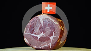 Delicious smoked tenderloin with small flag of Switzerland, piece of meat rotating on balck background.