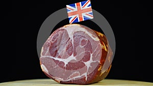 Delicious smoked tenderloin with small flag of United Kingdom, piece of meat rotating on balck background.