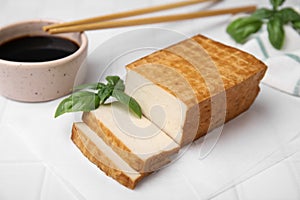 Delicious smoked tofu, soy sauce and basil on tiled table