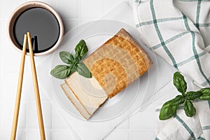 Delicious smoked tofu, soy sauce and basil on tiled table, flat lay