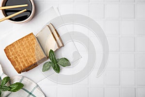 Delicious smoked tofu, soy sauce and basil on tiled table, flat lay. Space for text