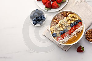 Delicious smoothie bowl with fresh berries, banana, coconut flakes and granola on white marble table, flat lay. Space for text