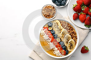 Delicious smoothie bowl with fresh berries, banana, coconut flakes and granola on white table, flat lay. Space for text