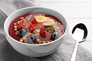 Delicious smoothie bowl with fresh berries, banana and granola on white wooden table, closeup
