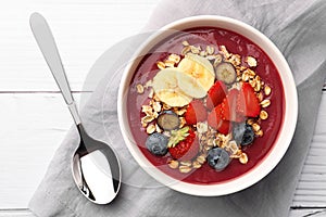 Delicious smoothie bowl with fresh berries, banana and granola on white wooden table, flat lay