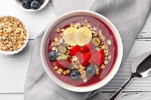 Delicious smoothie bowl with fresh berries, banana and granola on white wooden table, flat lay