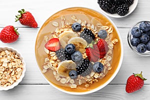 Delicious smoothie bowl with fresh berries, banana and oatmeal on white wooden table, flat lay