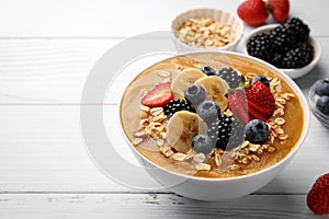 Delicious smoothie bowl with fresh berries, banana and oatmeal on white wooden table. Space for text