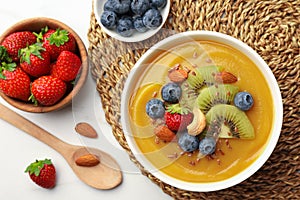 Delicious smoothie bowl with fresh berries, kiwi and nuts on white table, flat lay