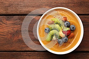 Delicious smoothie bowl with fresh berries, kiwi and nuts on wooden table, top view. Space for text