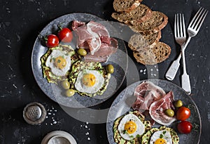 Delicious snack or appetizer - prosciutto, zucchini fritters, fried quail eggs, tomatoes, olives on a dark table, top view. Medite