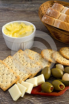 Delicious Snack, Crackers, Olives, Butter, Cheese and Bread in a Basket on Wood Table