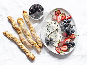 Delicious snack - gorgonzola cheese, grapes, strawberries, olives and sesame breadsticks on a light background, top view