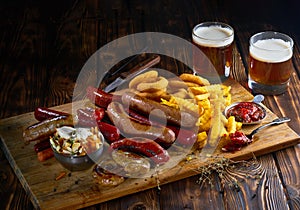 Delicious snacks with grilled sausages, fried potato, onion rings and two glasses of beer on wooden board in rustic