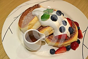 Delicious Souffle Pancake with Maple Syrup, Fresh Whipped Cream and Mix Berries Served on white Plate