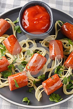 Delicious spaghetti hot dog in the form of spiders and ketchup close-up in a plate on the table. Vertical top view