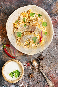 Delicious spicy chicken biryani in ceramic bowl on rustic background with spices, Indian or Pakistani food. Top view