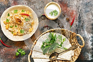 Delicious spicy chicken biryani in ceramic bowl on rustic background with spices, Indian or Pakistani food. Top view