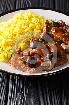 Delicious stewed beef fricando with gravy and wild mushrooms served with yellow rice closeup. vertical