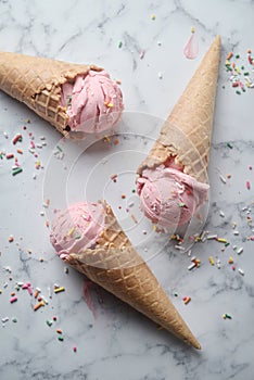 Delicious strawberry ice cream cone decorated with sugar rainbow sprinkles on marble background. top view