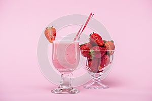 Delicious strawberry milkshake in glass with straw and fresh strawberries in bowl