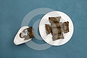 Delicious stuffed grape leaves traditional doom Mediterranean cuisine Dolma on white plate with sauce. Top view. Blue background