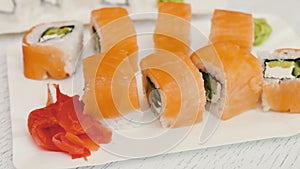 Delicious sushi with salmon, cheese, wasabi, pink ginger, soy sauce on a stylish white wooden background