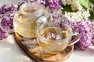 Delicious sweet herbal tea with lilac scent, glass cup and teapot with hot drink