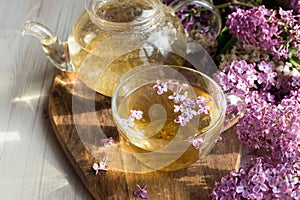 Delicious sweet herbal tea with lilac scent, glass cup and teapot with hot drink