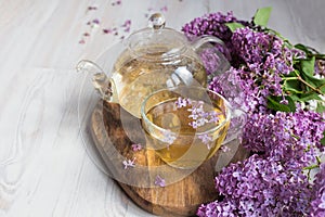 Delicious sweet herbal tea with lilac scent, glass cup and teapot with hot drink