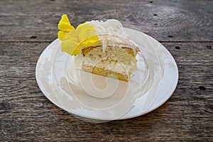 Delicious sweet white fresh coconut cake with beautiful yellow trumpet flower decoration on white ceramic plate on wooden table