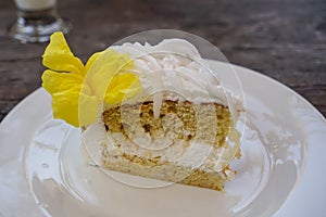 Delicious sweet white fresh homemade coconut cake with beautiful yellow trumpet flower decoration on white ceramic plate on wooden