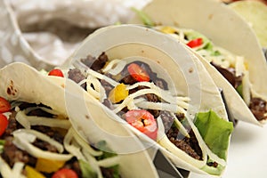 Delicious tacos with fried meat, vegetables and cheese on white table, closeup