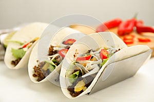 Delicious tacos with fried meat, vegetables and cheese on white wooden table, closeup