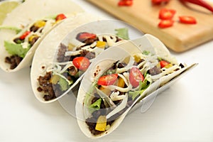 Delicious tacos with fried meat, vegetables and cheese on white wooden table, closeup