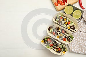 Delicious tacos with fried meat, vegetables and cheese on white wooden table, flat lay. Space for text