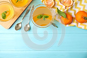 Delicious tangerine jelly and fresh fruits on light blue wooden table, flat lay. Space for text