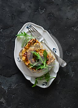 Delicious tapas - a piece of zucchini frit potatoes with arugula salad on a dark background, top view