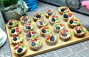 Delicious tartlets with creme cheese and fresh berries on wooden board.